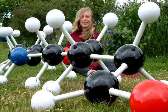 A girl sitting on grass behind a giant molecular model of nylon